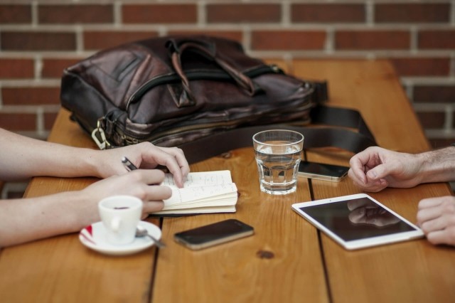 Hands, mobiles and tablets on a desk during a meeting