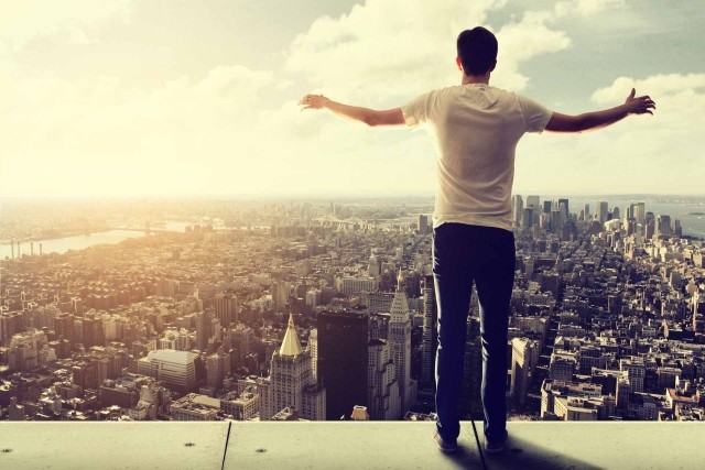 Man standing on a ledge looking over the skyline of a city