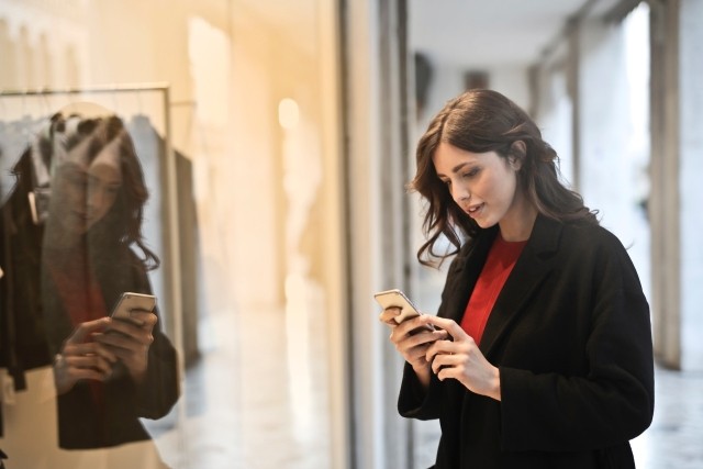 A woman standing by glass looking at her smartphone