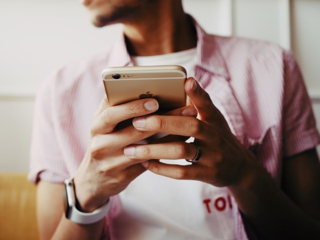 A man in a pink shirt using his cell phone to send an SMS